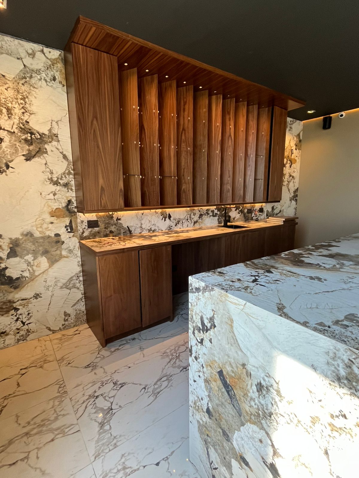 Cocina con muro e isla de mármol veteado y carpintería de nogal iluminada